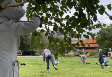 Eine Person in einem hellen Anorak steht zusammen mit einem kleinen Baum und schaut auf ein paar Menschen, die sich frei auf einer Weise auf dem Steinplatz in Berlin bewegen